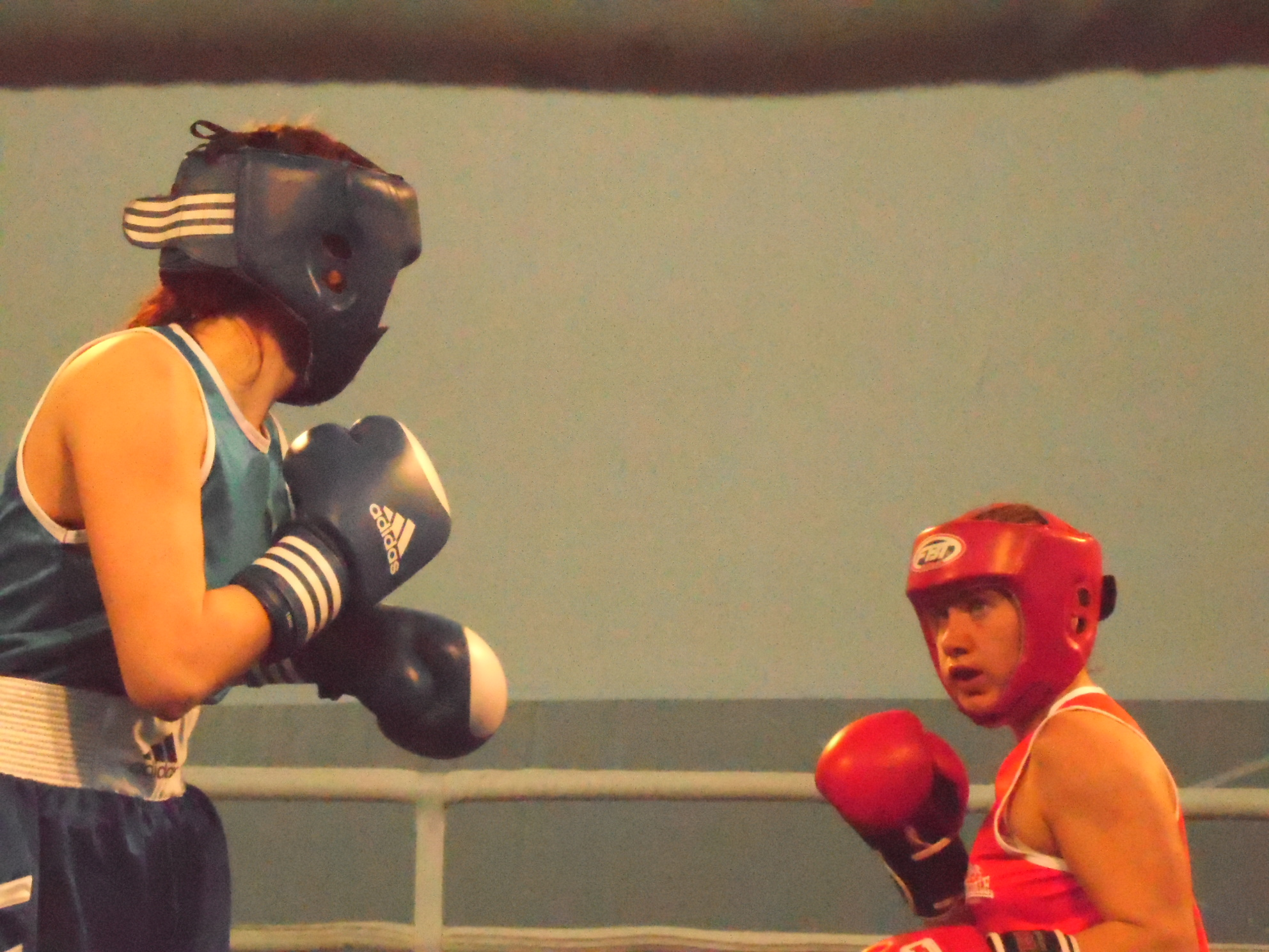 A women dressed in blue athletic attire and headgear (foreground) about to punch another woman wearing similar attire in red